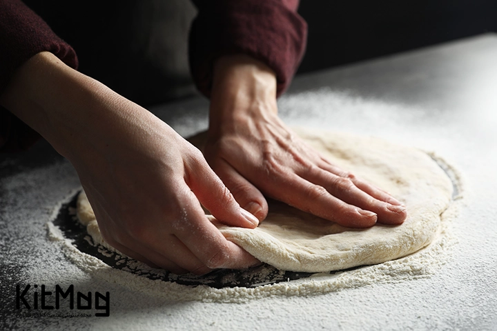 خمیر پیتزا که آشپز در حال ورز دادن آن است و قصد درست کردن پیتزا را دارد