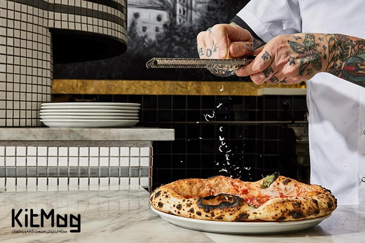 آشپز در حال ریختن پنیر پارمزان روی پیتزا ناپولیتن در آشپزخانه رستوران می باشد