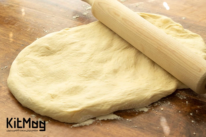 خمیر پیتزا صاف شده با وردنه روی یک میز چوبی
