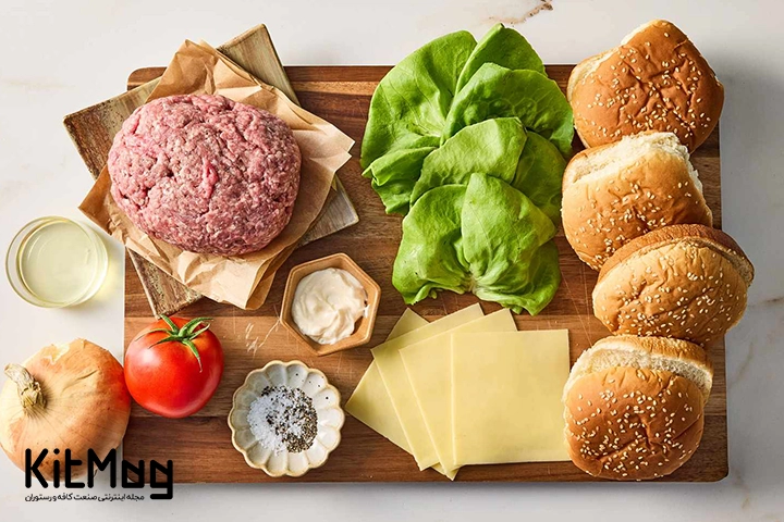مواد اولیه لازم برای تهیه همبرگر رستورانی که روی یک تخته چوبی قرار گرفته است
محتویات روی آن اعم از نان برگر گوجه کاهو سس پیاز روغن پخت و گوشت تازه چرخ شده می باشد