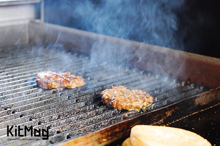 گریل گازی که روی آن چند عدد برگر قرار \رفته است و در حال دود کردن است
