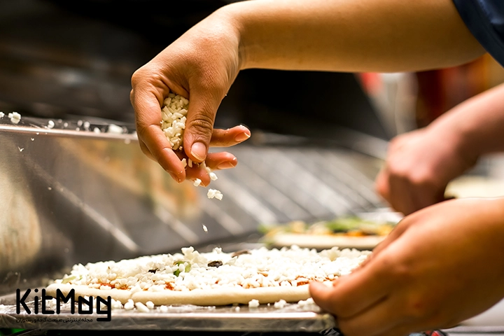 آشپز در حال ریختن تاپینگ های مورد استفاده در پیتزا و پنیر پیتزا روی خمیر می باشد