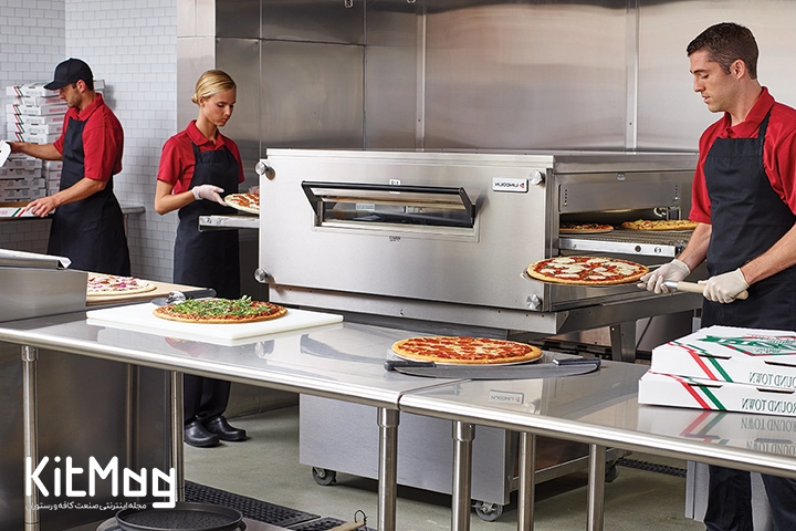 کارمندان یک پیتزا فروشی در حال پخت و بسته بندی پیتزا در یک رستوران بزرگ با لباس قرمز آستین کوتاه و پیشبند مشکی