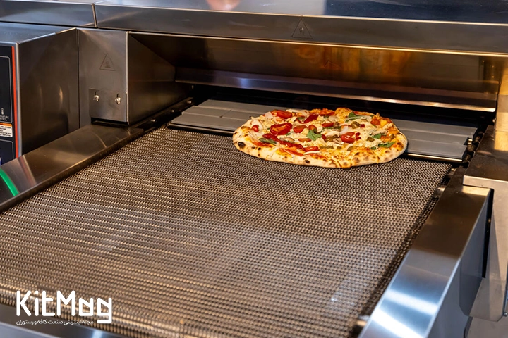 یک پیتزا پخته شده در حال عبور از فر ریلی پیتزا از نمای نزدیک می باشد