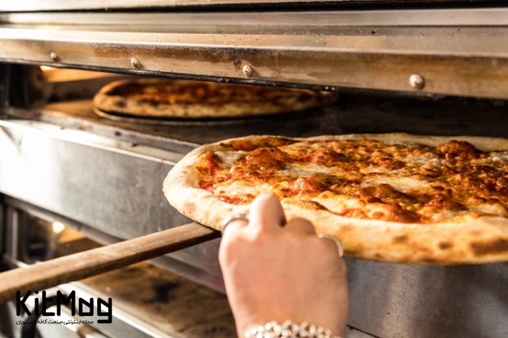 آشپز در حال تست کراست پیتزا ایتالیایی از داخل فر پیتزا می باشد که با پارو پیتزا پیتزا را خارج کرده است