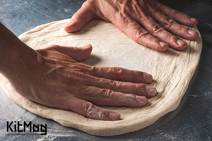 آشپز در حال پهن کردن خمیر پیتزا روی میز استیل می باشد