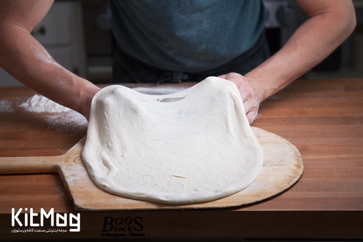 آشپز در حال پهن کردن خمیر پیتزا روی یک پاروی چوبی می باشد