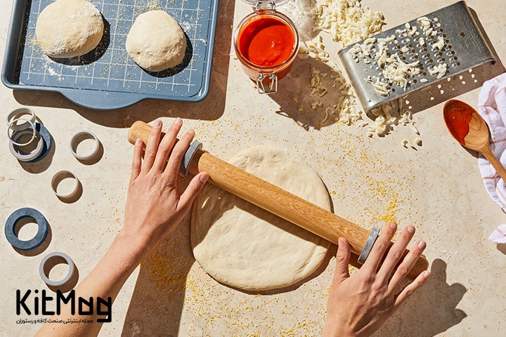 یک آشپز در حال پهن کردن خمیر پیتزا روی میز با وردنه یا به اصطلاح رولینگ پین
