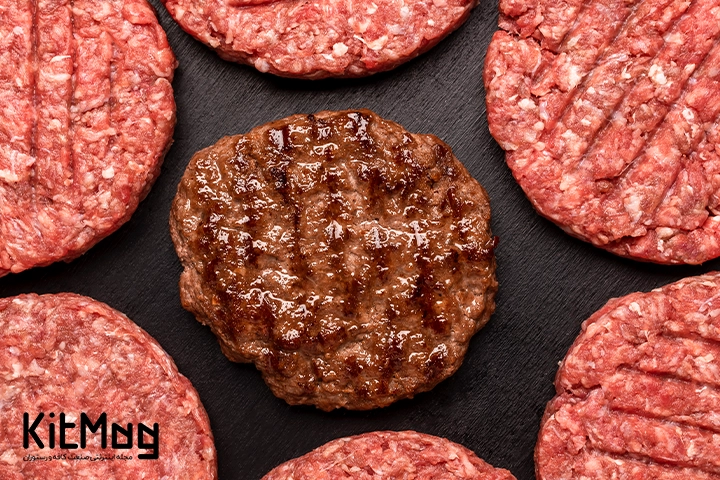 یک عدد برگر پخته شده که وسط تصویر قرار گرفته است و همبرگر های نپخته در کنار آنها قرار دارند