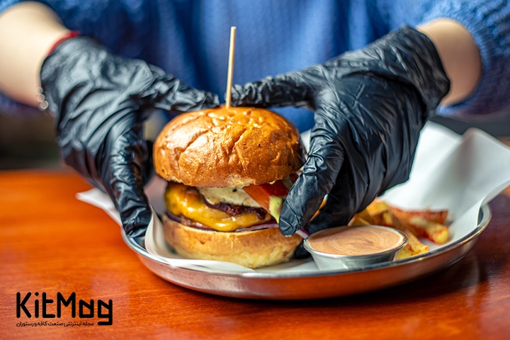 یک آشپز در رستوران مشغول سرو کردن یک برگر رستورانی لذیذ و حیجان انگیز است که یک برگر است که داخل سینی فلزی قرار گرفته است و یک چوب از وسط آن رد شده است