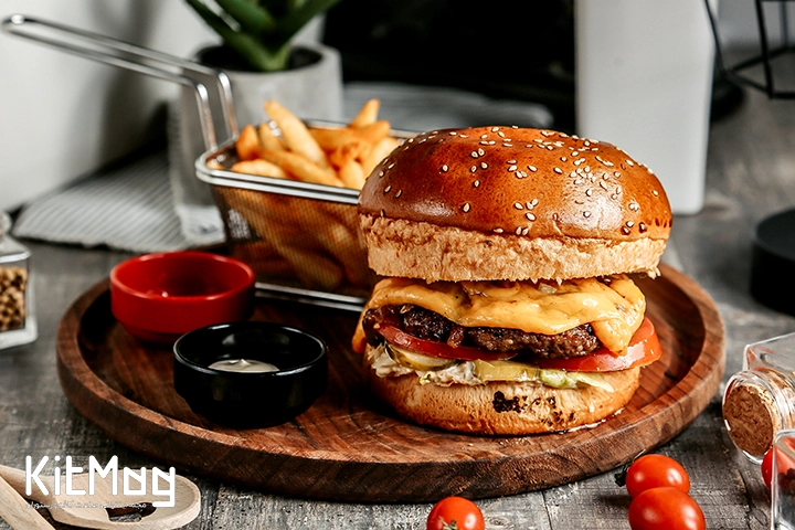 یک همبرگر که داخل یک سینی چوبی قرار گرفته است و داخل کاسه های مختلف آن سس سفید و قرمز ریخته شده است