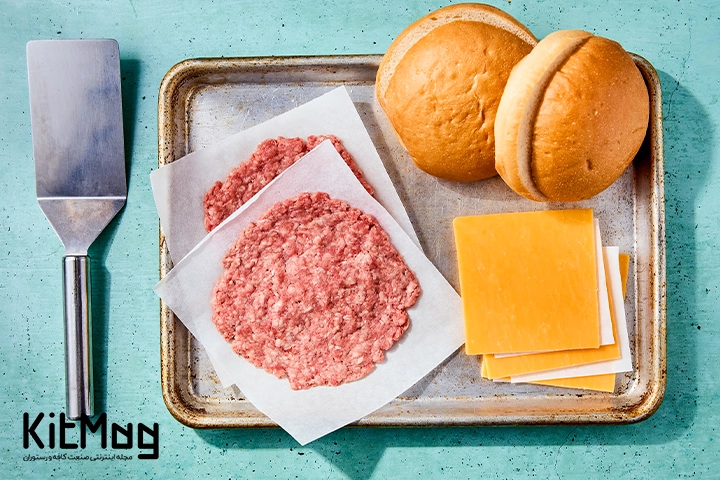 تعداد گوشت پتی یا همان قالبی همبرگر در کنار اسپاچولا نان همبرگری و پنیر چدار بسته بندی شده آماده برای تهیه همبرگر