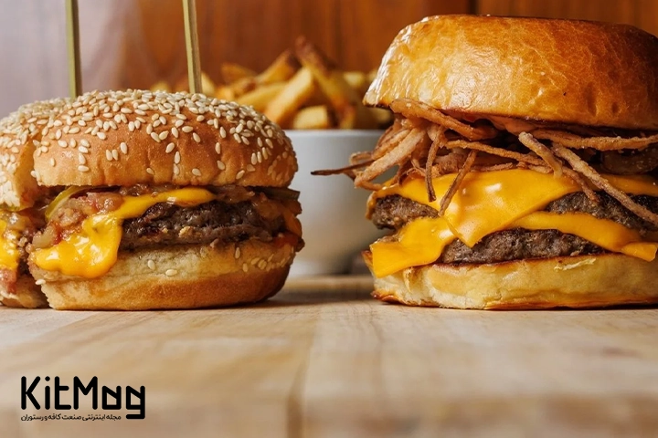 یک عدد چیز برگر در سمت چپ تصویر و یک عدد دبل چیزبرگر در سمت راست تصویر دیده می شود که روی یک میز چوبی قرار گرفته است