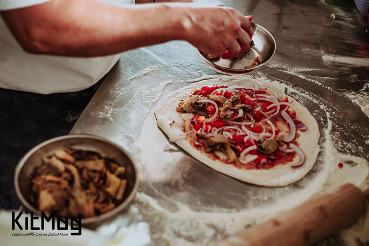 اشتباهات رایج در تهیه پیتزا
یک آشپز در حال قرار دادن تاپینگ های پیتزا روی آن