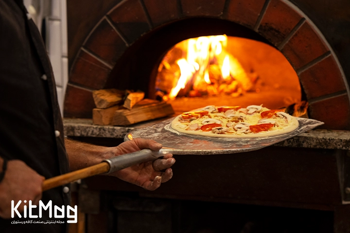 یک آشپز در حال قرار دادن خمیر پیتزا داخل تنور پیتزا می باشد