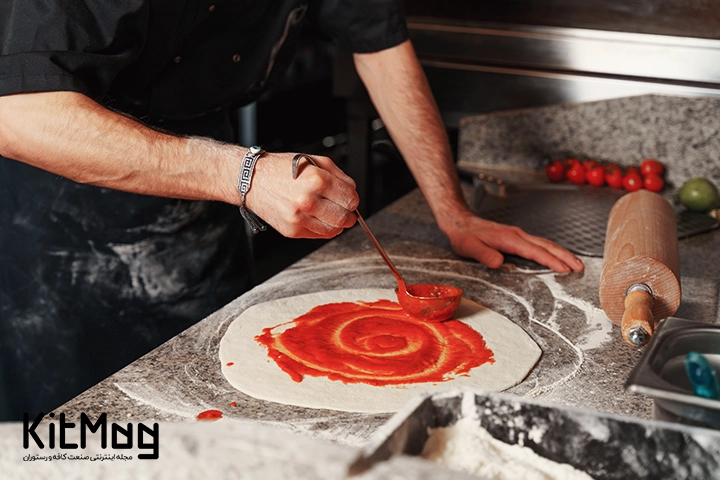 آشپز پیتزا فروشی در حال پهن کردن و ریختن سس پیتزا روی آن می باشد