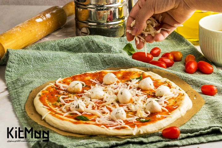 آشپز در حال ریختن پنیر پارمزان روی پیتزا ایتالیایی می باشد پیتزا روی یک پارچه نخی قرار گرفته است