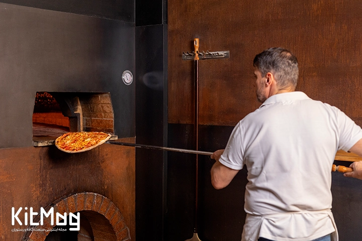آشپز در حال قرار دادن پیتزا با پارو مخصوص پیتزا داخل فر گنبدی می باشد