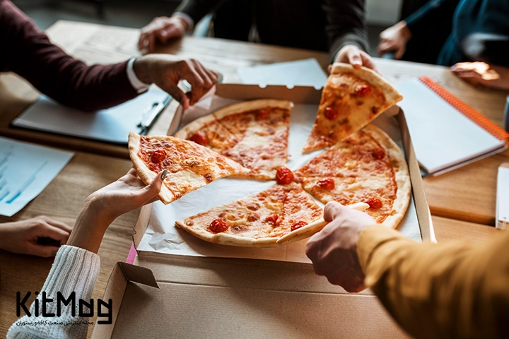 دستهای مشتریان رستوران پیتزا فروشی در یک پیتزا در حال برداشتن اسلایس های پیتزا