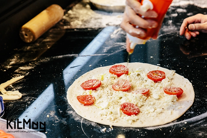 یک آشپز در حال ریختن سس زیتون روی پیتزا و خمیر آن روی میز رستوران