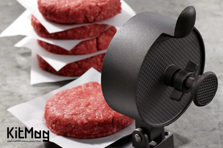 همبرگر زن مشکی دستی یا منوآل که در کنار آن تعدادی پتی همبرگر آماده دیده میشود