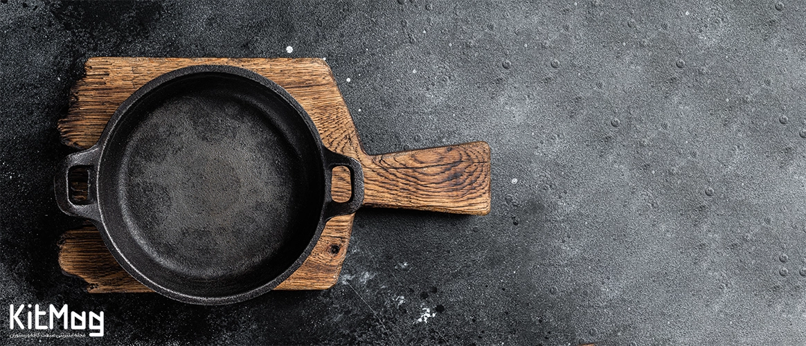 تمیز کردن ظروف چدنی یک ظرف چدنی که روی میز یک رستوران قرار گرفته است و پس زمینه طوسی آن با یک تخته چوبی در تصویر دیده می شود