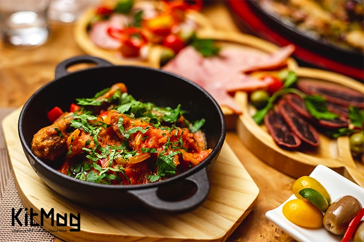 تابه چدنی که در آن سبزیجات همراه با مواد دیگر پخته است و مقداری مرغ سرخ شده در کنار آنها ریخته شده است