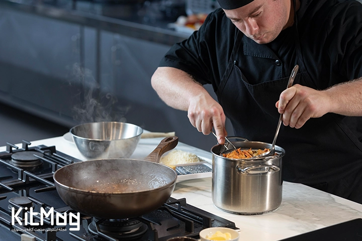 یک آشپز در حال پخت و پز در آشپزخانه یک رستوران مدرن و بزرگ می باشد این آشپز از ظروف و تابه چدنی دسته دار در حال استفاده می باشد و همچنین درحال خارج کردن مواد از داخل قابلمه استیل می باشد