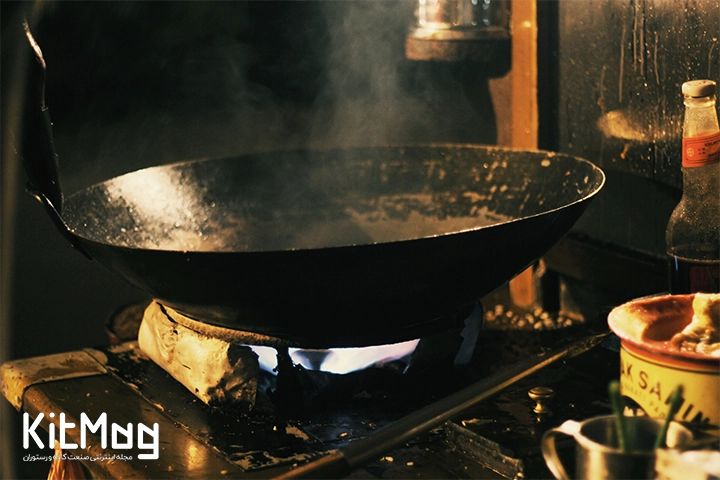 یک تابه ووک چدنی که در رستوران در آن مشغول پخت و پز هستند این تابه روی یک اجاق مخصوص ووک قرار گرفته است