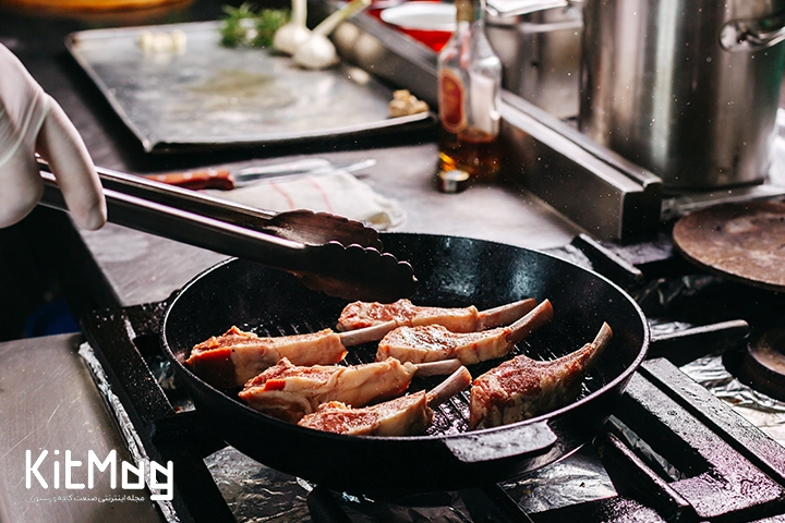 یک آشپز در حال پخت تکه های گوشت استیک با استخوان داخل تابه چدنی می باشد که در محیط رستوران می باشد