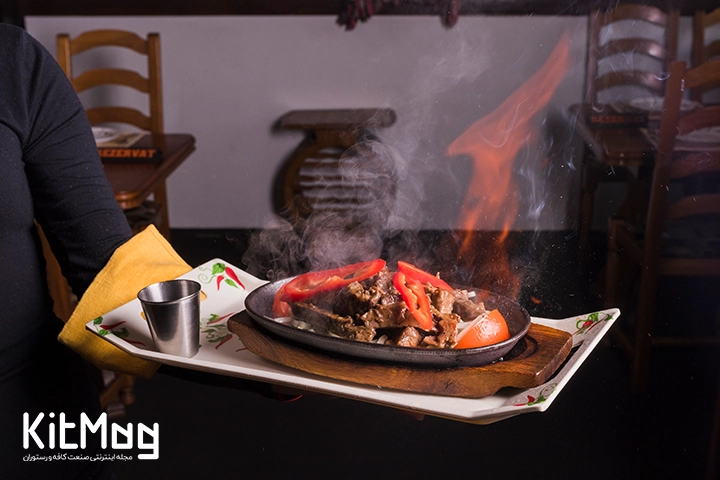 استیک گوشت که در حال دود کردن و با پخت کامل به خمراه مخلفات کامل آماده سرو مشتری در رستوران می باشد