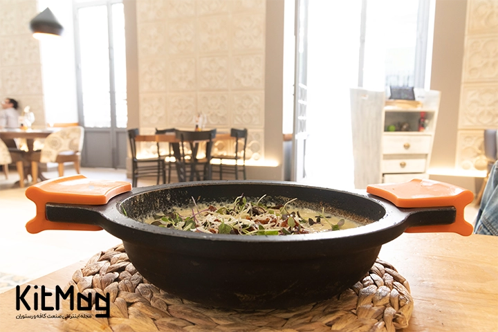 تابه چدنی با دسته مخصوص حرارت که داخل آن مواد غذایی به همراه خامه پخته شده است و دسته های آن دارای حفاظ مخصوص حرارت می باشند و همچنین روی یک حرارت گیر حصیری قرار گرفته است