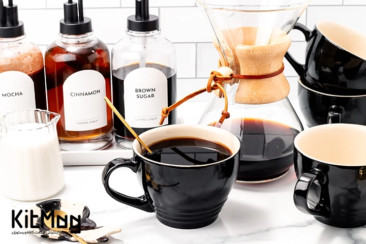 یک لیوان قهوه آمریکانو که در کافه قرار دارد و یک لیوان شیر و کمکس با قهوه داخل آن در عکس دیده می شود