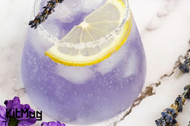 موکتل لیموناد اسطوخودوس (Lavender Lemonade) که داخل لیوان گرد پایه کوتاه ریخته شده است و روی آن با برگ اسطوخودوش و نعنا تزئین شده است و رنگ آن بنفش است