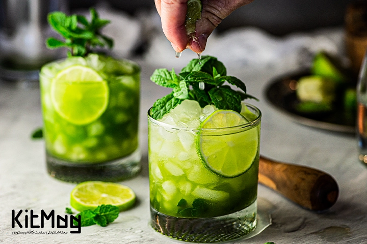 موکتل ماچا و نعناع (Matcha Mint Mocktail) نوشیدنی بسیار خوشمزه و جذاب که طعمی شبیه به موهیتو دارد با لیمو و نعنا تزئین شده است و دو عدد لیوان از آن روی یک صفحه قرار گرفته و عکاسی شده است