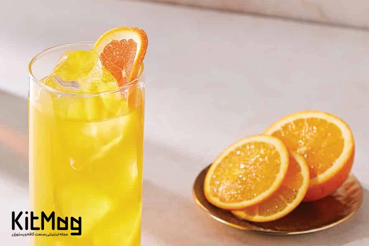 موکتل مانگو تورمریک تانگو (Mango Turmeric Tango) که در یک لیوان پایه بلند ریخته شده است و با تکه های پرتقال تزئین شده است