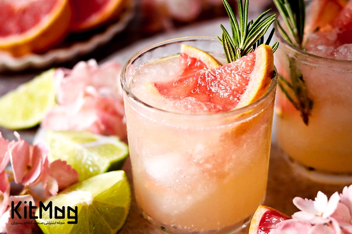 موکتل اسپریتز گریپ فروت و رزماری (Grapefruit Rosemary Spritz) که داخل یک لیوان پایه بلند ریخته شده است و با یخ و تکه های گریپ فروت و رزماری تزئین شده است