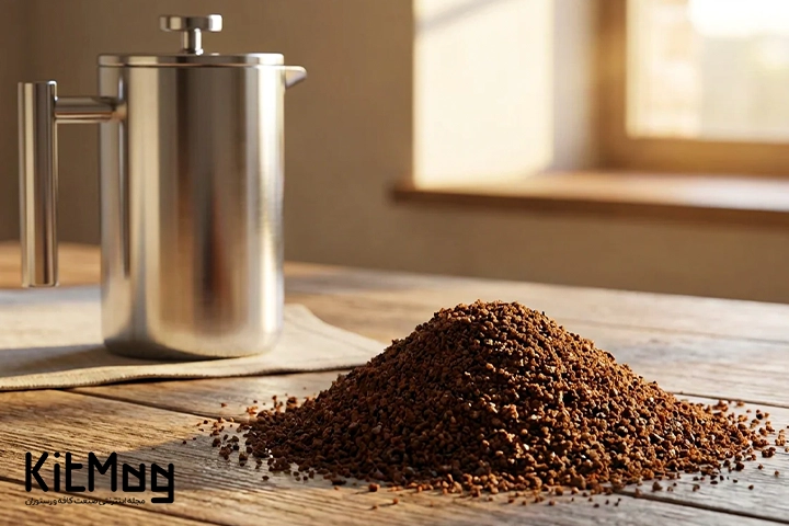آسیاب درشت  (Coarse Ground Coffee)
که روی یک میز چوبی ریخته شده است و یک فرنچ پرس استیل روی میز چوبی قرار گرفته است