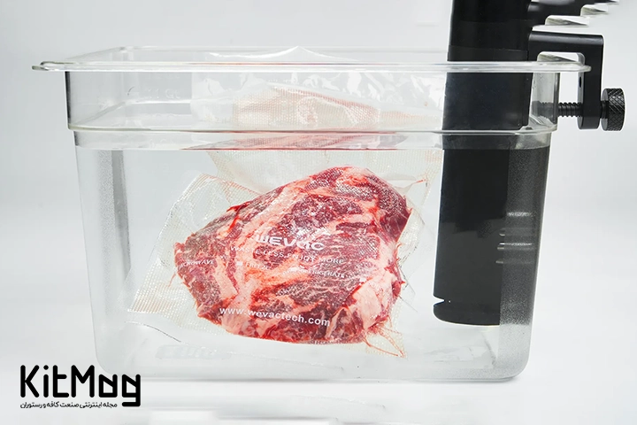 دستگاه Sous Vide یا سووید که از نمای نزدیک قابل مشاهده می باشد و روی یک میز چوبی قرار گرفته است و در حال سیرکولیت کردن مواد غذایی در فضای خلا می باشد