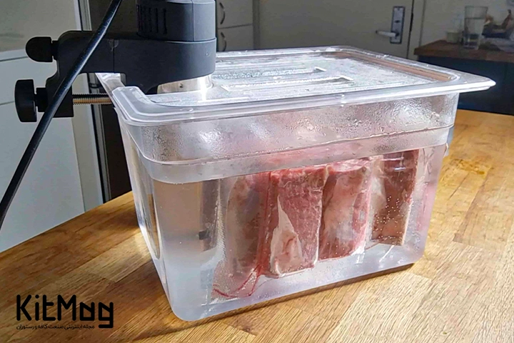 دستگاه Sous Vide یا سووید که از نمای نزدیک قابل مشاهده می باشد و روی یک میز چوبی قرار گرفته است و در حال سیرکولیت کردن مواد غذایی در فضای خلا می باشد
