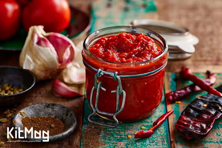 سس تند مخصوص رستورانی یا هات سس که روی تخته چوب رستورانی و در داخل یک جار ریخته شده است و سیر پوست کنده نشده و فلفل های مخصوص در کنار آن دیده می شود